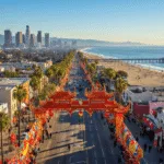 "Aerial view of Los Angeles with Chinatown's Lunar New Year decorations in foreground, downtown skyline, Santa Monica Pier, surfers in the Pacific Ocean, and Griffith Observatory on a clear February afternoon"