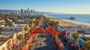 "Aerial view of Los Angeles with Chinatown's Lunar New Year decorations in foreground, downtown skyline, Santa Monica Pier, surfers in the Pacific Ocean, and Griffith Observatory on a clear February afternoon"