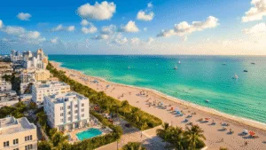 "Aerial view of Miami Beach with Art Deco buildings, palm trees, colorful beach umbrellas, hotel pools, yachts, and beachgoers on a sunny day"