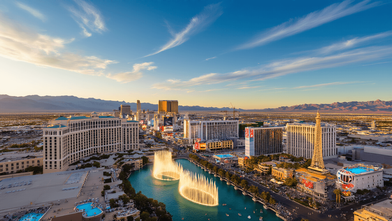 "Panoramic aerial view of Las Vegas Strip during golden hour, showing bustling pool parties, performing Bellagio fountains, illuminated cityscape, and the contrast with the serene desert mountains sprinkled with spring wildflowers."