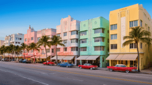 "Art Deco buildings in pastel colors along Ocean Drive in Miami during golden hour, prominently featuring geometric facades, window eyebrows and chrome accents, with neon signs and palm trees lining the street"